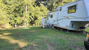 A white RV with a ramp and a small deck, parked in a grassy area with trees in the background. - Beav-o-rama nights (Fayetteville)