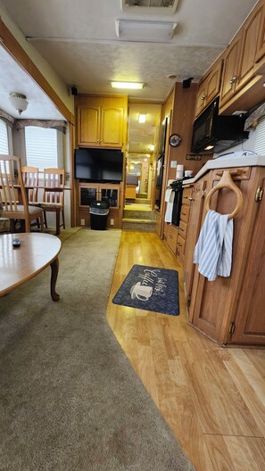 A compact RV kitchen with wooden cabinets, a microwave, and a dining area with chairs.