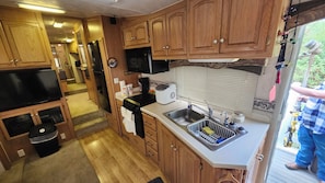 A compact kitchen with wooden cabinets, a microwave, a toaster, and a sink. - Beav-o-rama nights (Fayetteville)