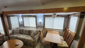 A compact RV interior with a sofa, dining table, and chairs. - Beav-o-rama nights (Fayetteville)