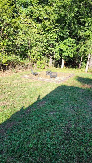 An outdoor seating area with metal chairs and a table, surrounded by grass and trees.