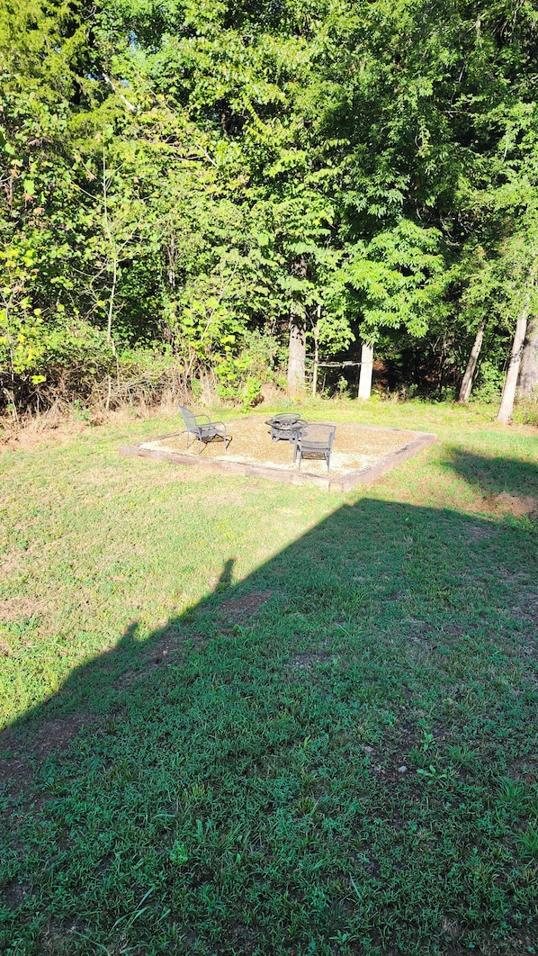 An outdoor seating area with metal chairs and a table, surrounded by grass and trees. - Beav-o-rama nights (Fayetteville)