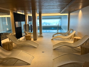 Ein moderner Innenbereich zum Entspannen mit weißen Liegestühlen, einem Pool und Blick auf eine gebirgige Landschaft.