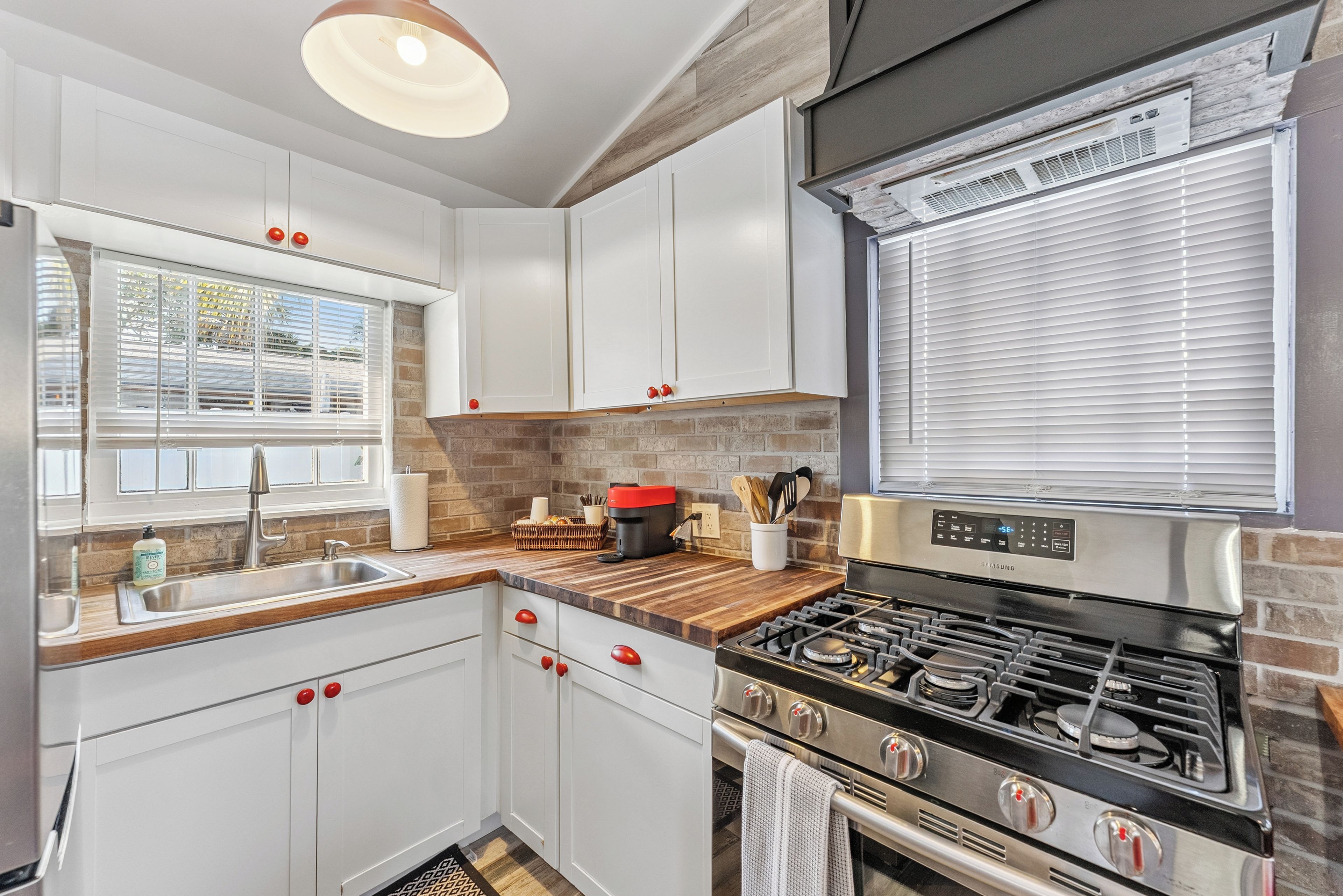 A modern kitchen with white cabinets, a stainless steel stove, and a window with blinds.