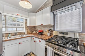 Une cuisine moderne avec des meubles blancs, une cuisinière en acier inoxydable et une fenêtre équipée de stores.