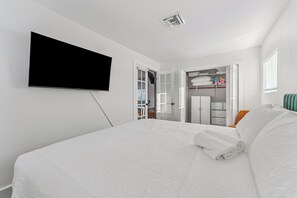 A hotel room with a bed, a flat-screen TV mounted on the wall, a walk-in closet, and a window with blinds. - Tropical Pool Retreat / Heated Pool & Hot Tub / Minutes to Beach & Downtown (lake worth beach)