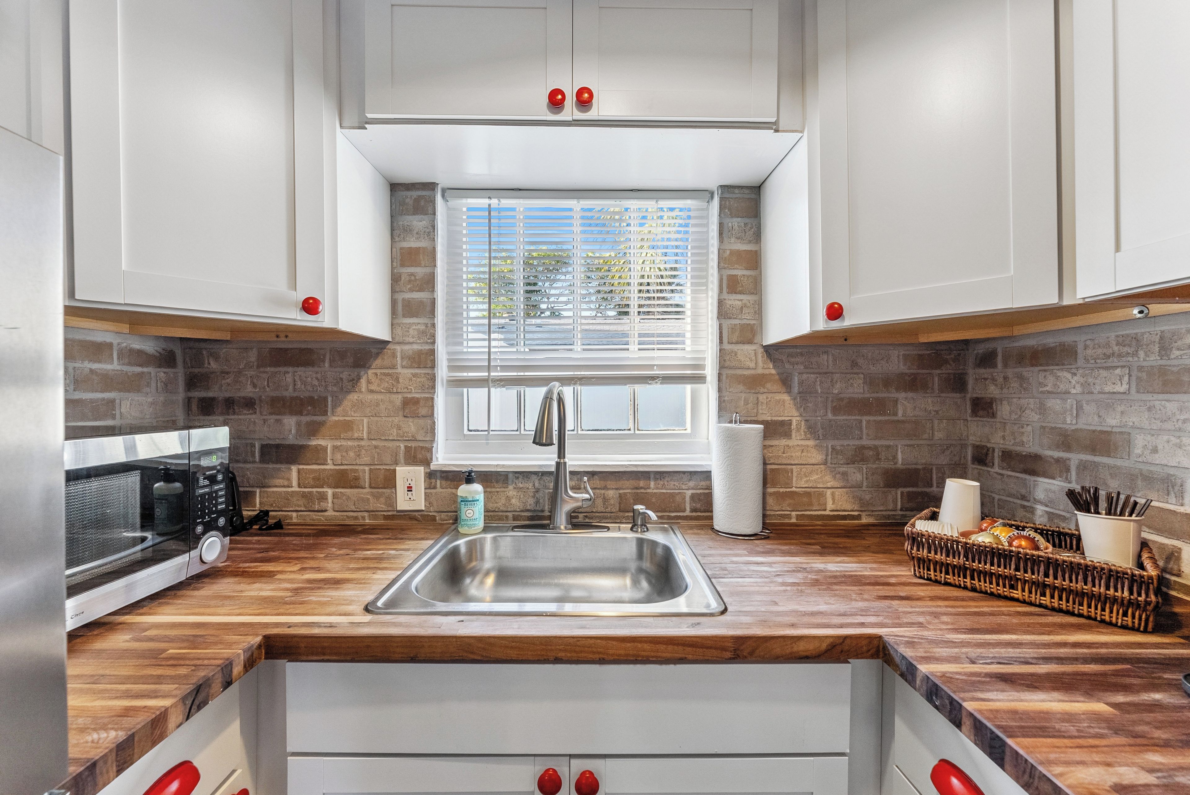 A kitchen with a wooden countertop, stainless steel sink, and white cabinets.