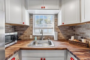 A kitchen with a wooden countertop, stainless steel sink, and white cabinets. - Tropical Pool Retreat / Heated Pool & Hot Tub / Minutes to Beach & Downtown (lake worth beach)