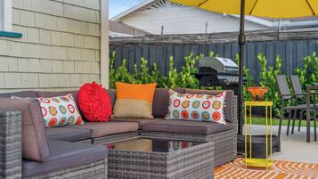 An outdoor seating area with a wicker sofa, colorful cushions, and a yellow umbrella.