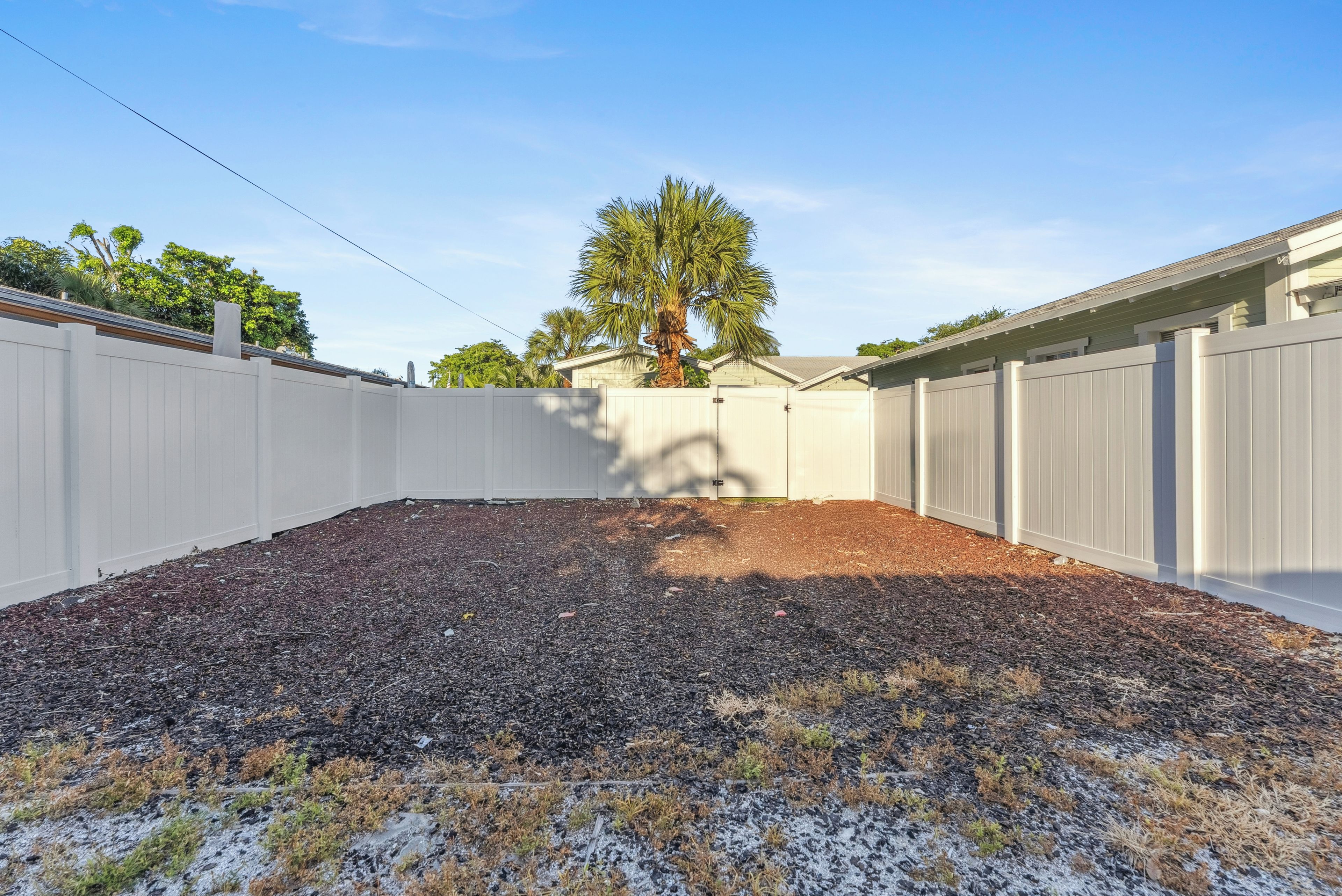 A backyard with a wooden fence, a tree, and a mulched area.
