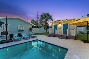 A backyard with a swimming pool, lounge chairs, a small deck, and a house with a blue door. - Tropical Pool Retreat / Heated Pool & Hot Tub / Minutes to Beach & Downtown (lake worth beach)