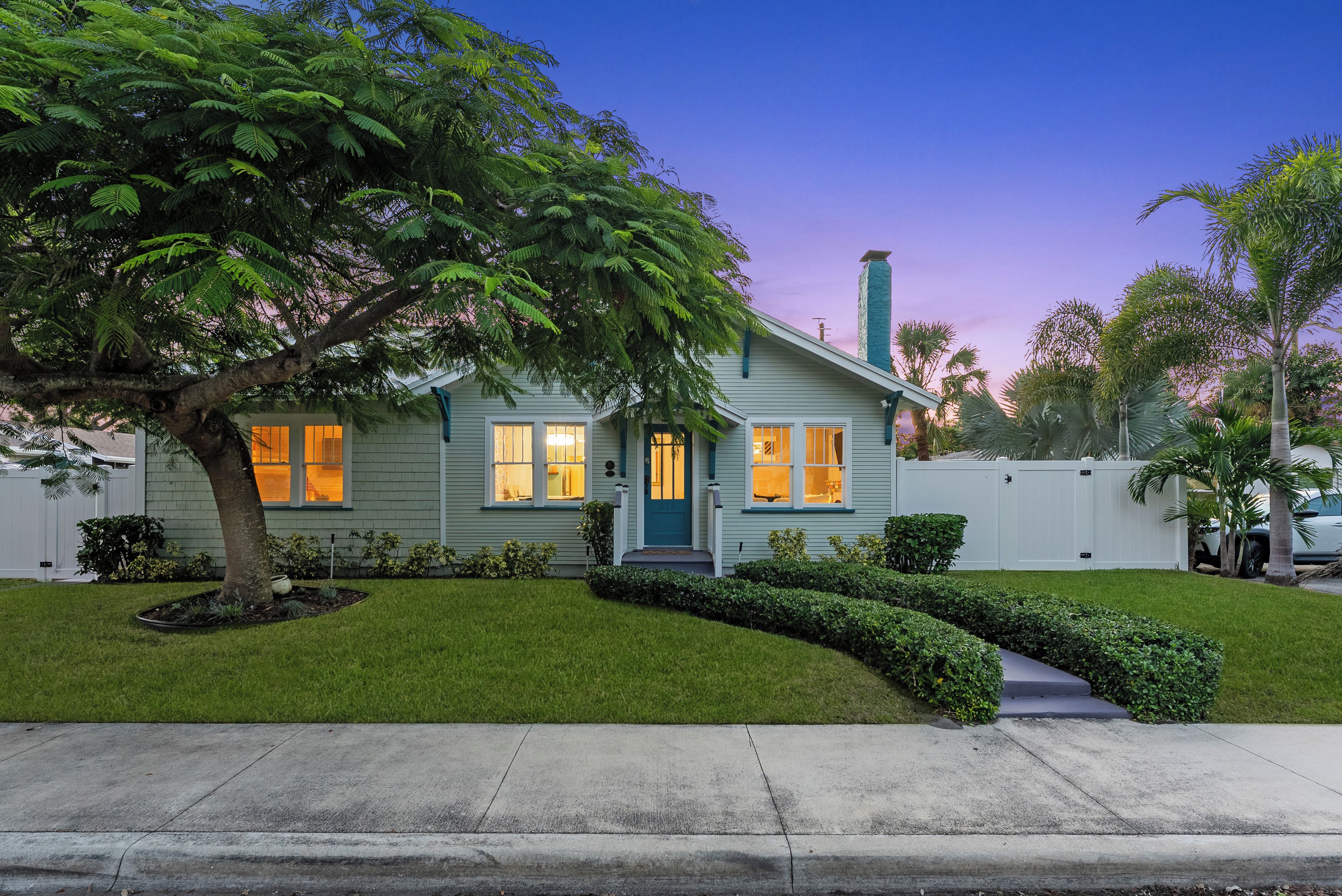 A two-story house with a front yard, a tree, and a white fence.