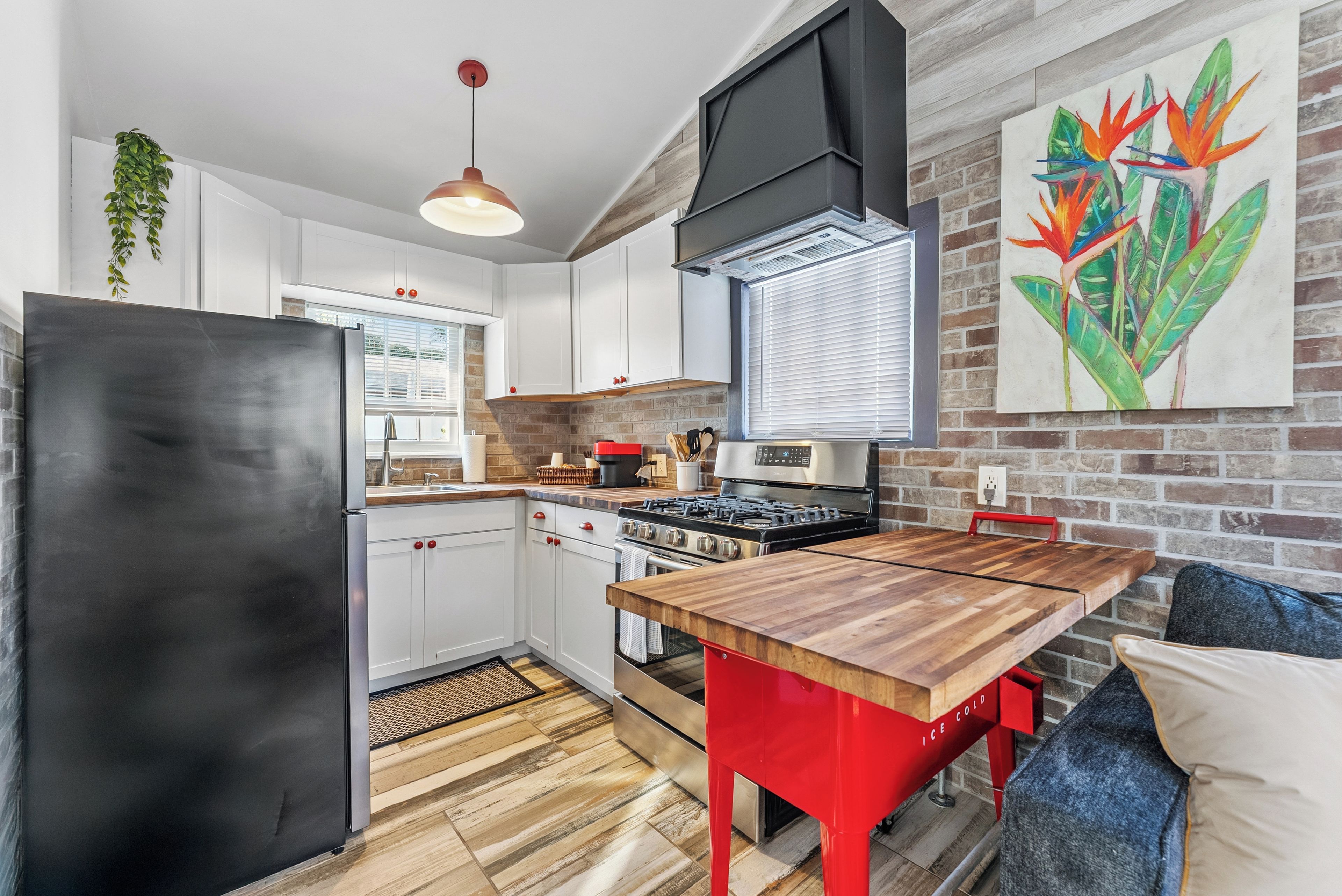 A modern kitchen with white cabinets, a black refrigerator, a red dining table, and a brick wall.