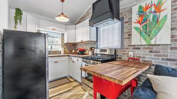 A modern kitchen with white cabinets, a black refrigerator, a red dining table, and a brick wall.