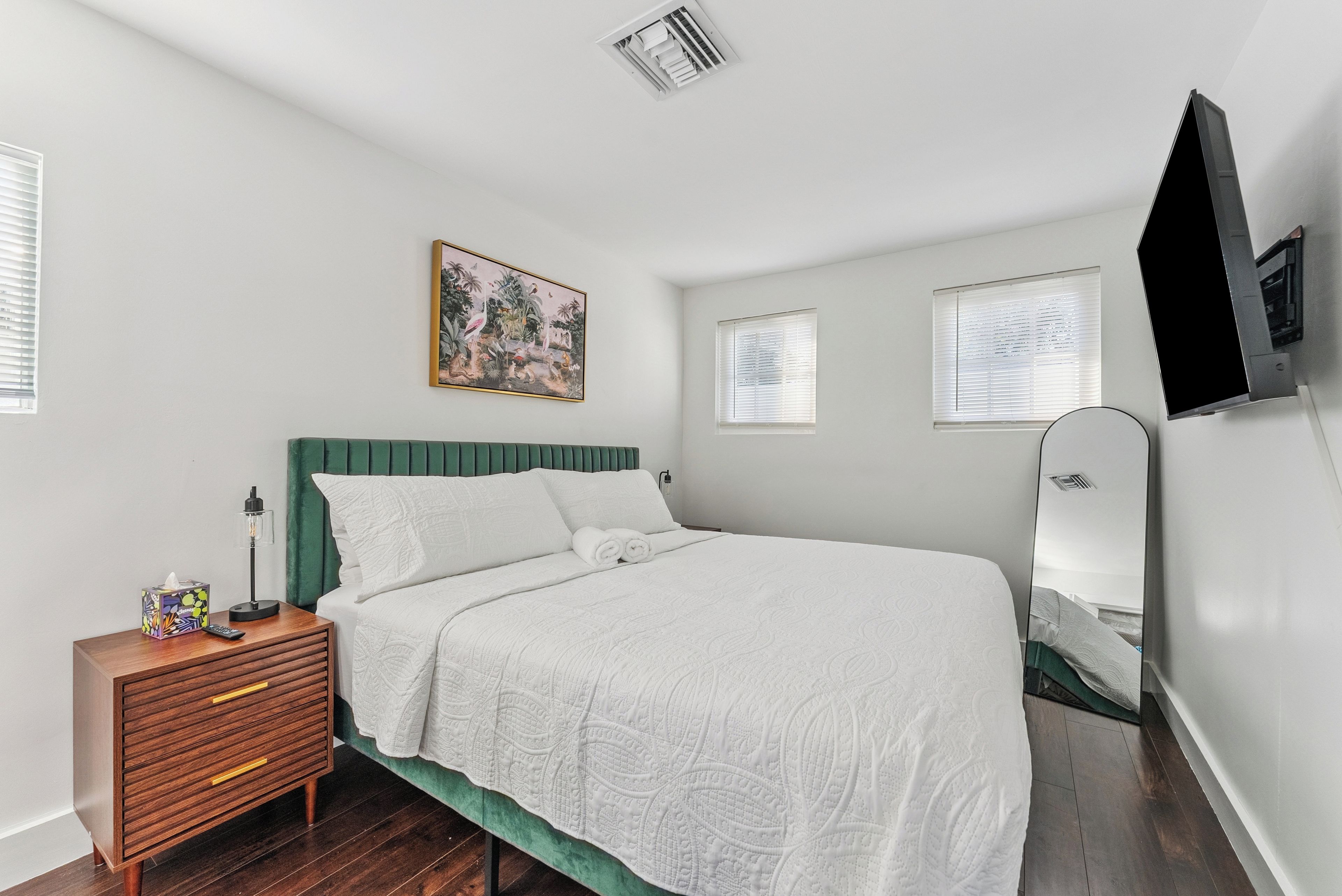 A bedroom with a bed, a bedside table, a mirror, and a painting on the wall.