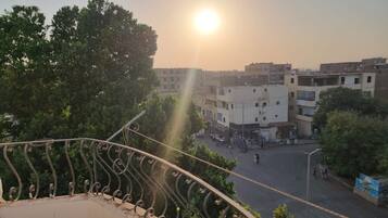 Un balcon doté d’une rambarde en métal, donnant sur une rue bordée d’immeubles et d’arbres.