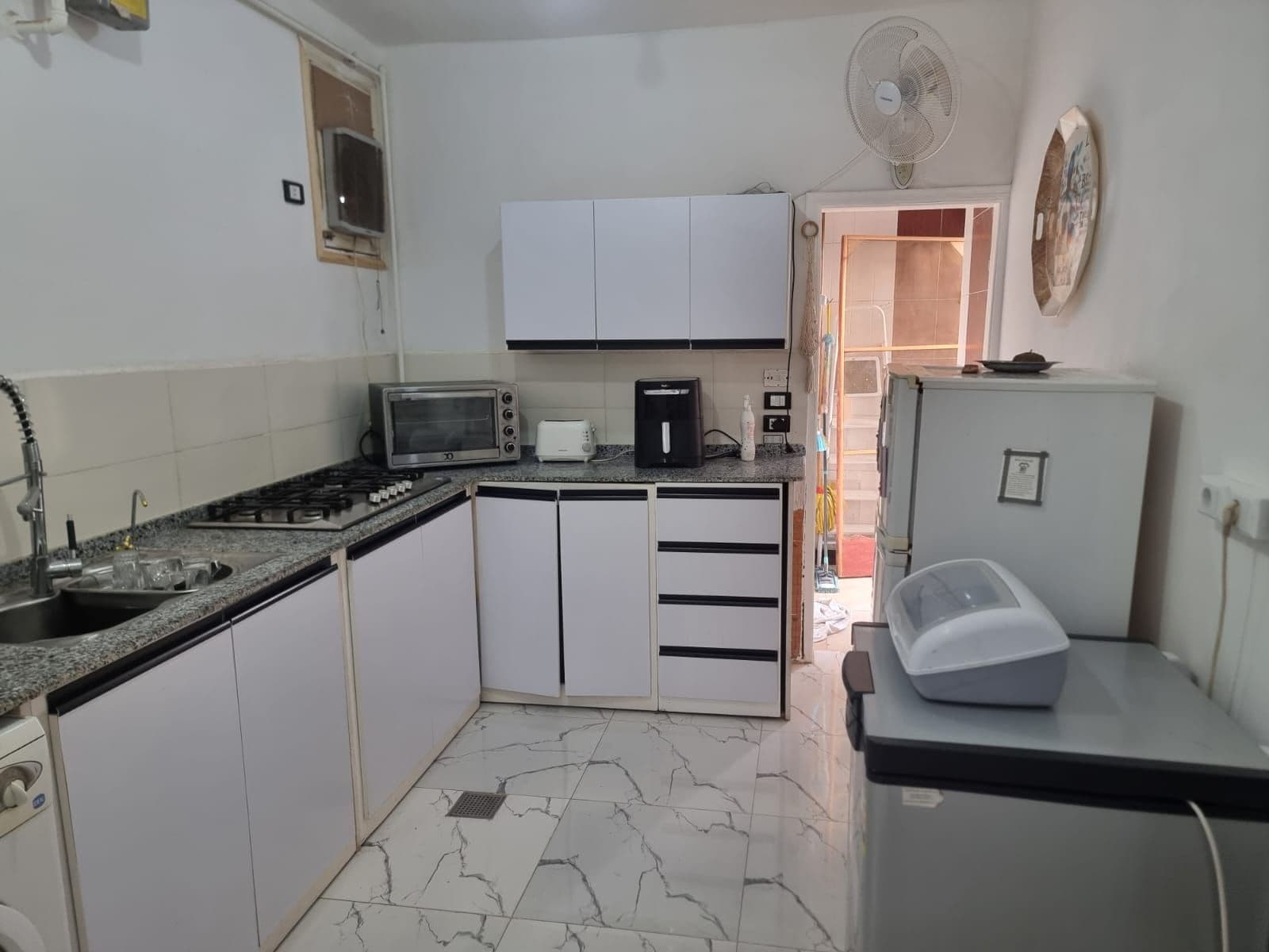 A compact kitchen with white cabinets, a microwave, a toaster, a sink, and a refrigerator.