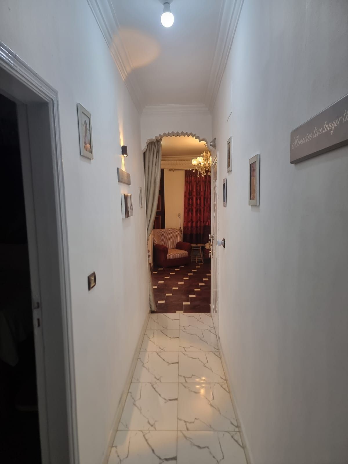 Un couloir doté d’un sol en marbre, d’un lustre et d’une enseigne accrochée au mur.