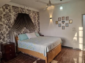 Een slaapkamer met een bed, nachtkastje, plafondventilator en wandlampen.