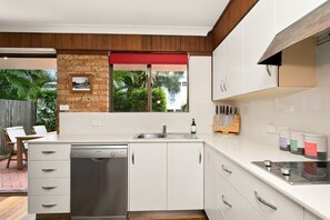 Eine moderne Küche mit weißen Schränken, einem Geschirrspüler, einem Einbauofen und einem roten Fensterrollo.