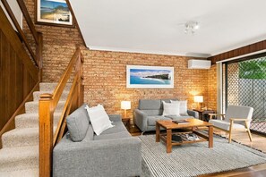 Ein Wohnzimmer mit Backsteinwand, einer Treppe, einem Sofa, einem Couchtisch und einem Sessel.