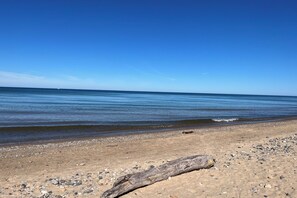 A beach with a clear sky, calm sea, and a large log in the foreground. - Luxury-private pool-across from beach (South Haven)