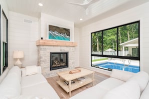 A modern living room with a fireplace, a pool view, and a large window. - Luxury-private pool-across from beach (South Haven)