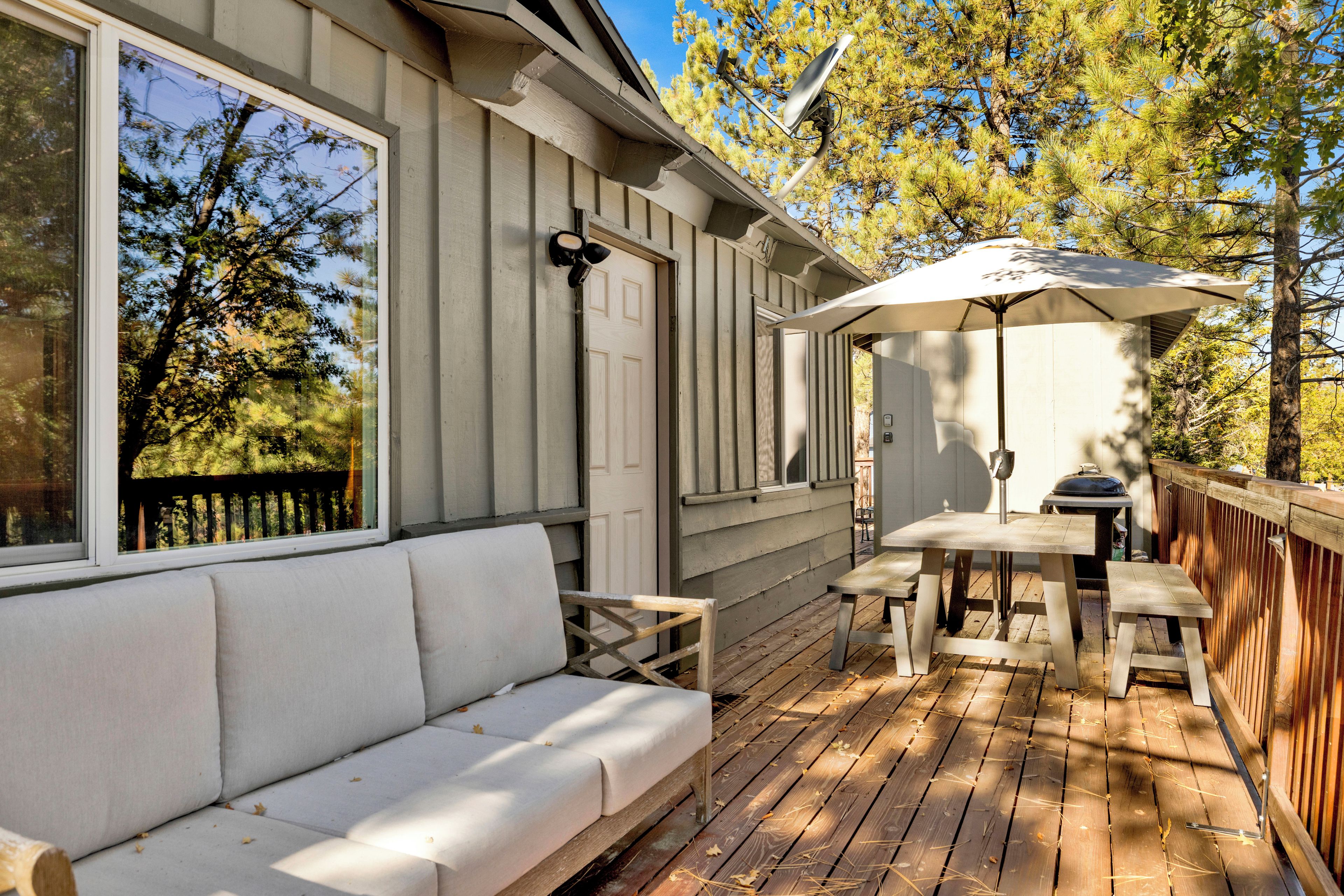 A wooden deck with a white outdoor sofa, a table with an umbrella, and a grill.