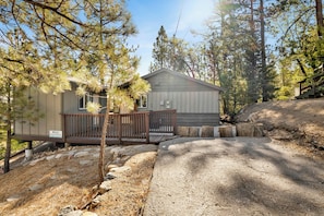 A cabin with a wooden deck and a small shed, surrounded by pine trees. - Cozy 2BR cabin with mountain views, fireplace, kitchen, and WiFi. (Big Bear Lake)