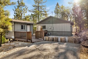 A cabin with a wooden deck and a small porch, surrounded by trees. - Cozy 2BR cabin with mountain views, fireplace, kitchen, and WiFi. (Big Bear Lake)