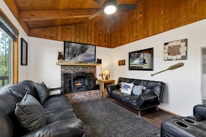 A cozy living room with a fireplace, leather sofa, and a mounted television. - Cozy 2BR cabin with mountain views, fireplace, kitchen, and WiFi. (Big Bear Lake)
