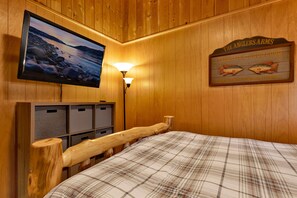 Ein Zimmer mit Holzboden, einem Bett, einem an der Wand montierten Fernseher, einem Schild, das frischen Fisch und gutes Essen anbietet, und einem Holzschrank mit Aufbewahrungsboxen.