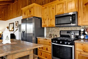 A kitchen with wooden cabinets, stainless steel appliances including a refrigerator, microwave, and stove, and a granite countertop. - Cozy 2BR cabin with mountain views, fireplace, kitchen, and WiFi. (Big Bear Lake)