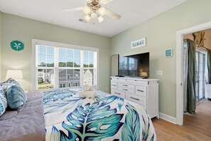 A bedroom with a bed, a TV, a dresser, and a window with blinds. - Footprints on the Fairway , 2BR Beach & Golf with Pool (Little River)