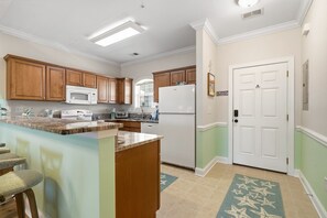 A kitchen with wooden cabinets, a white refrigerator, a microwave, and a built-in oven. - Footprints on the Fairway , 2BR Beach & Golf with Pool (Little River)
