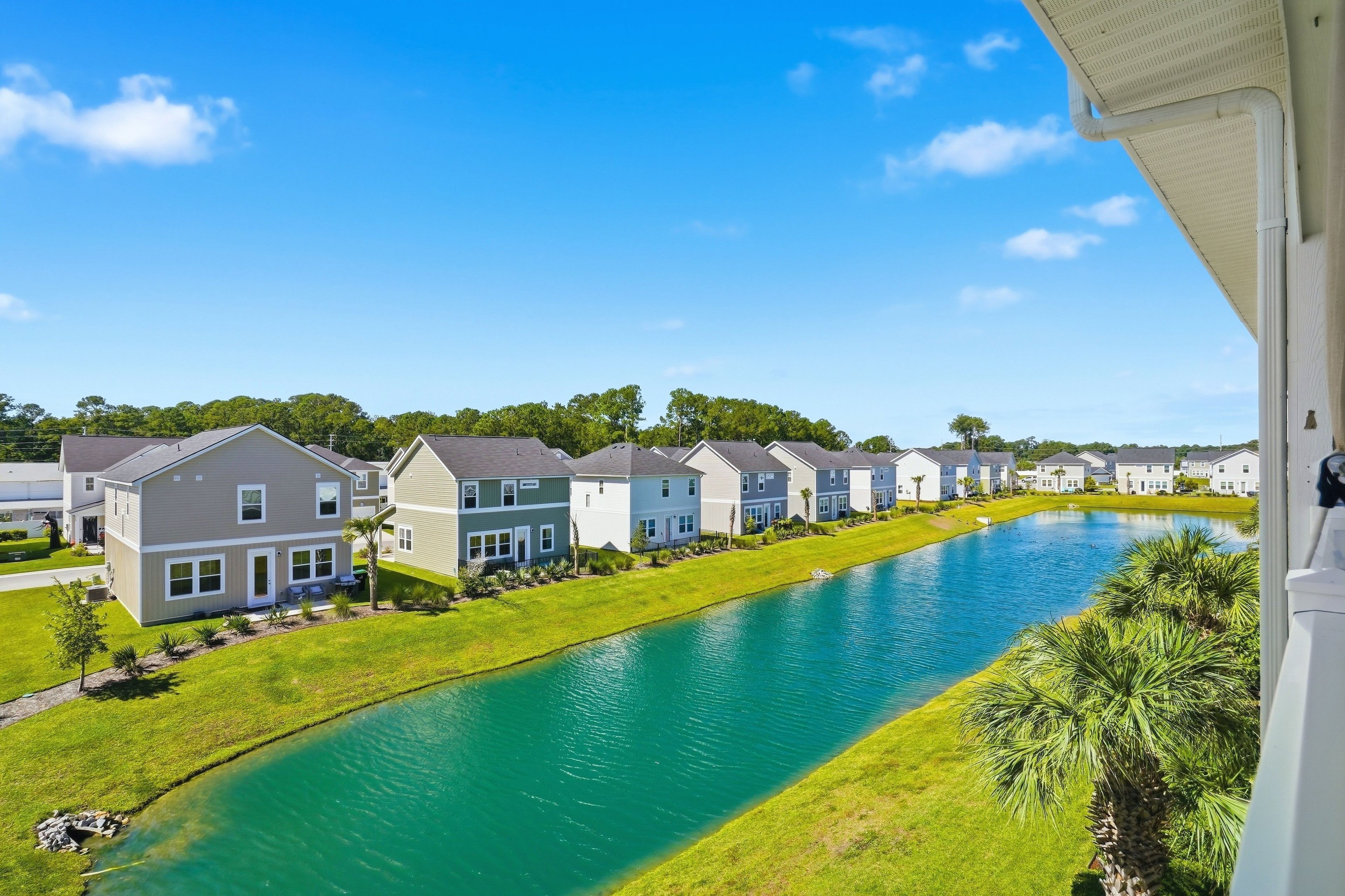 A residential area with houses aligned along a waterway, a clear sky, and a well-maintained lawn.