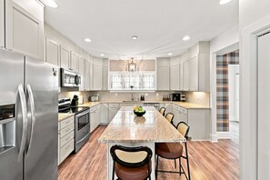 A modern kitchen with stainless steel appliances, a marble countertop, and a central island with seating. - 5 Min to Lucas Oil - Hot Tub - Arcade - Outdoor Movie - Propane Firepit (Indianapolis)
