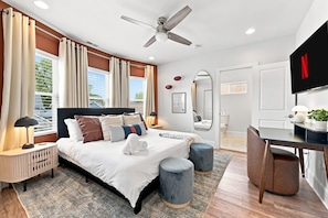 A modern bedroom with a bed, bedside lamps, a ceiling fan, a desk with a chair, and a flat-screen TV. - 5 Min to Lucas Oil - Hot Tub - Arcade - Outdoor Movie - Propane Firepit (Indianapolis)