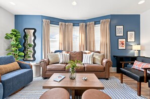 A modern living room with a brown leather sofa, a blue armchair, and a wooden coffee table. - 5 Min to Lucas Oil - Hot Tub - Arcade - Outdoor Movie - Propane Firepit (Indianapolis)