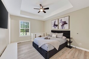 A bedroom with a bed, a ceiling fan, a window with blinds, and two wall-mounted artworks. - The Brick House on Elliott (Clarksville)