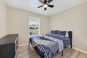Une chambre à coucher avec un lit, un ventilateur de plafond, une fenêtre avec des stores et une commode.