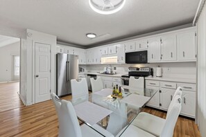 Une cuisine moderne avec des meubles blancs, des appareils en acier inoxydable et une table à manger en verre.