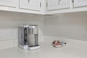A coffee maker on a white countertop with a small bowl of condiments and a cup. - The Brick House on Elliott (Clarksville)
