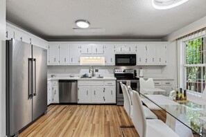 A modern kitchen with white cabinetry, stainless steel appliances, and a glass dining table. - The Brick House on Elliott (Clarksville)