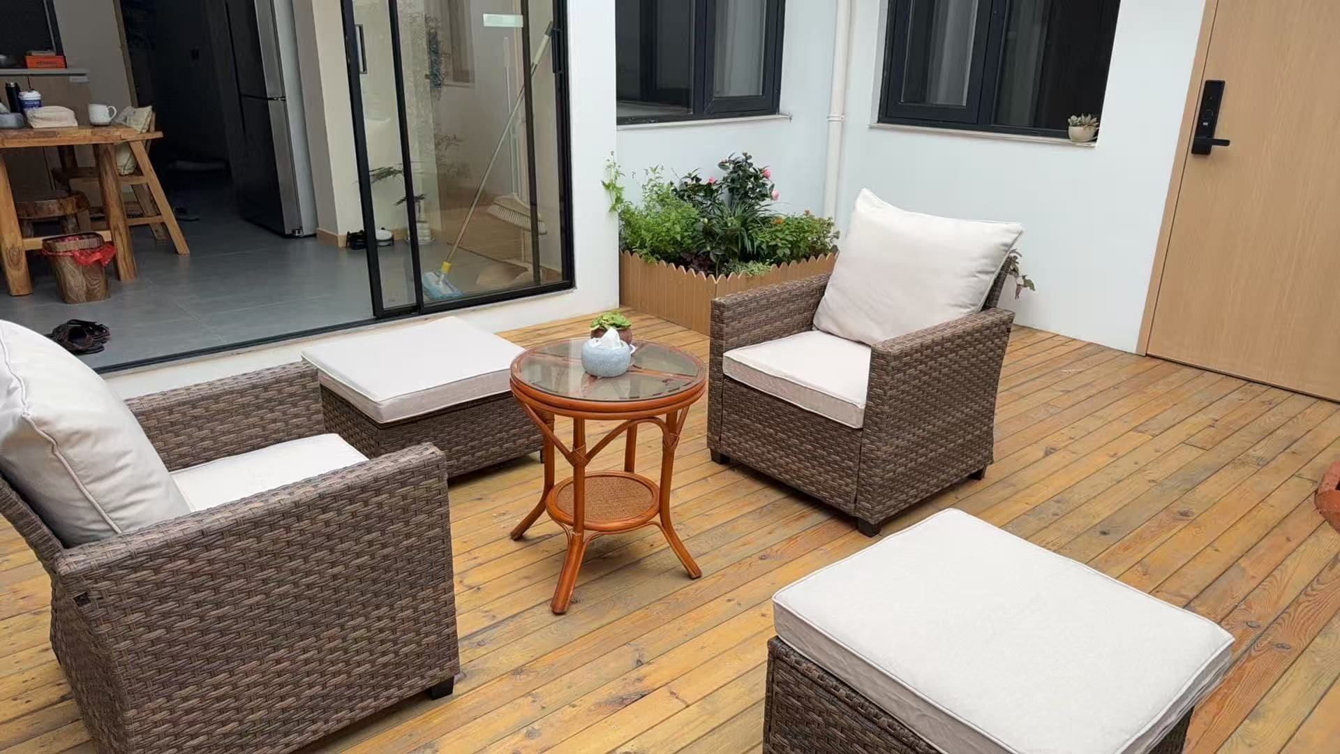 A cozy outdoor seating area with wicker furniture and a small table, surrounded by a wooden deck and a glass door leading to a patio.