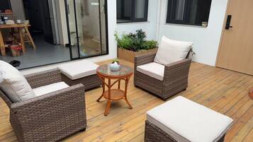 A cozy outdoor seating area with wicker furniture and a small table, surrounded by a wooden deck and a glass door leading to a patio.