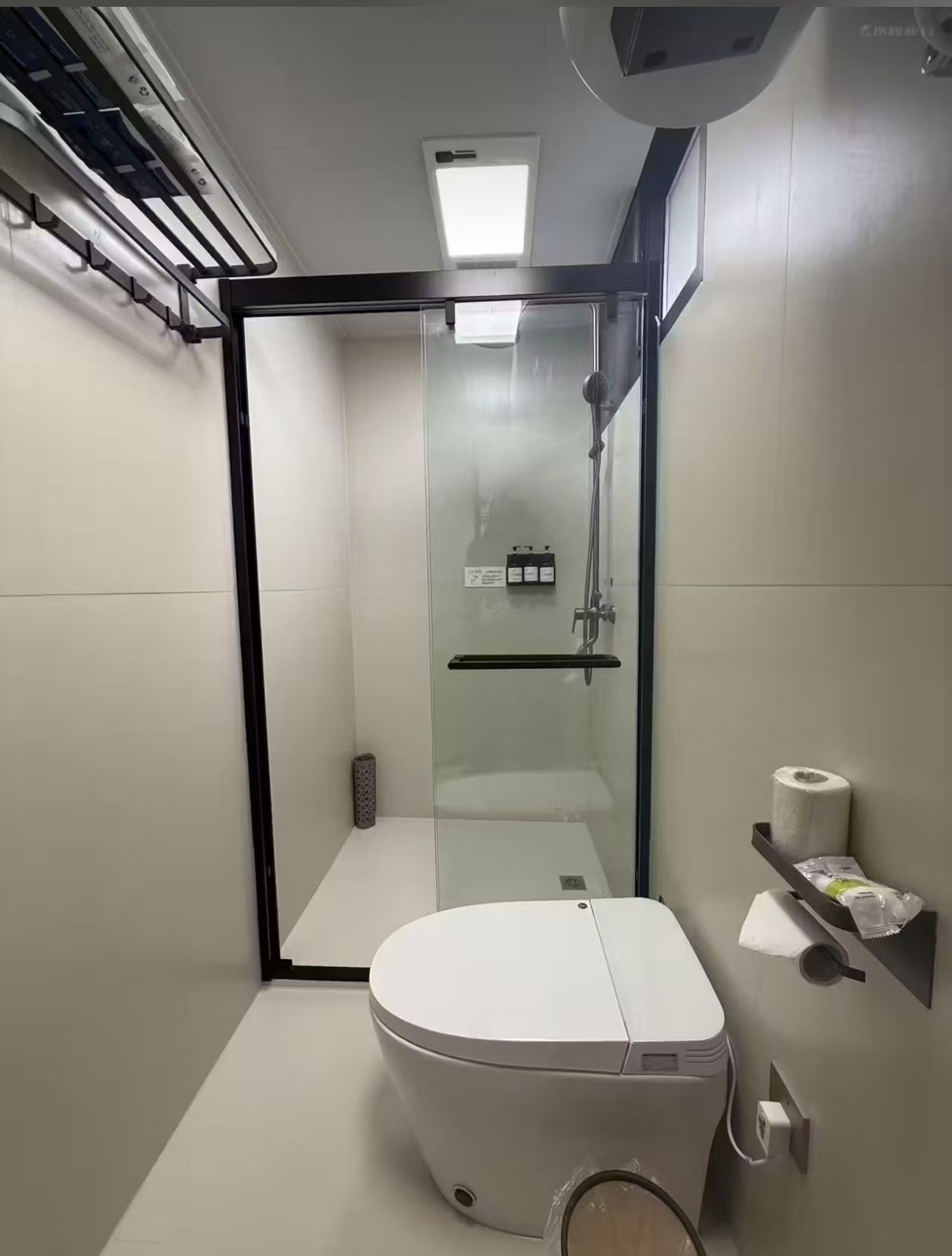 A modern bathroom with a glass-enclosed shower, a toilet, and a towel rack.
