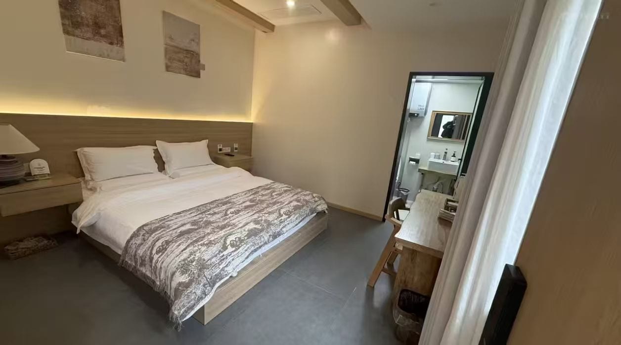 Una habitación de hotel con cama, mesita de noche, lámpara y espejo.
