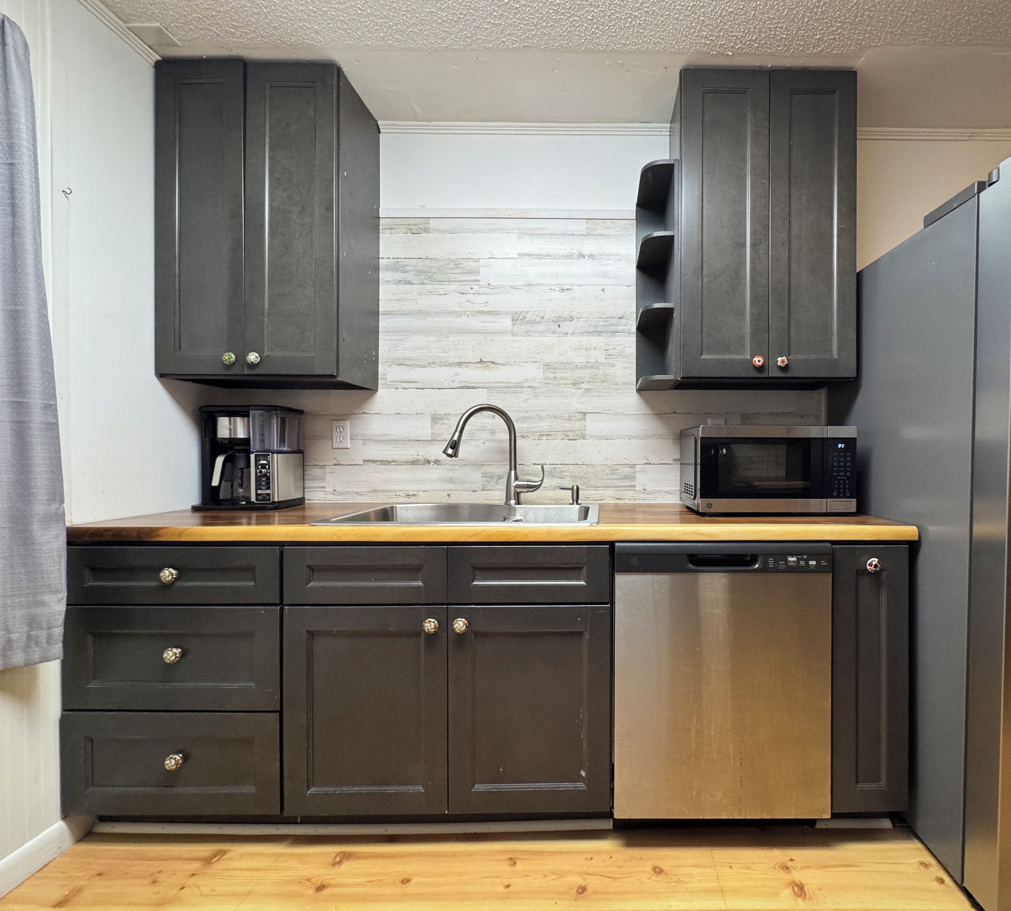 A kitchen with dark cabinets, a stainless steel dishwasher, a microwave, and a coffee maker.