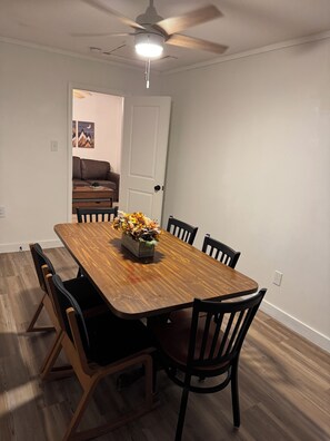 Un comedor con una mesa de madera, seis sillas y un ventilador de techo.